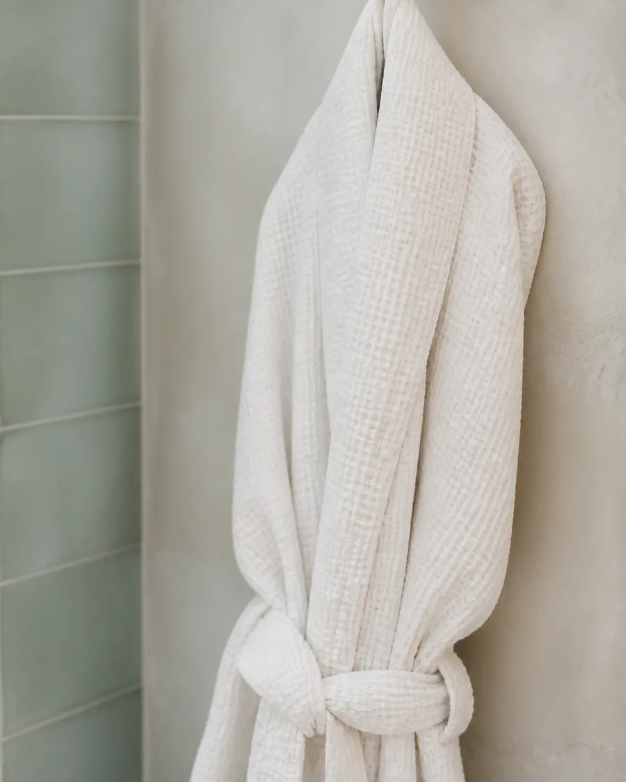 A folded white waffle robe hanging on a matte black hook against pale plaster