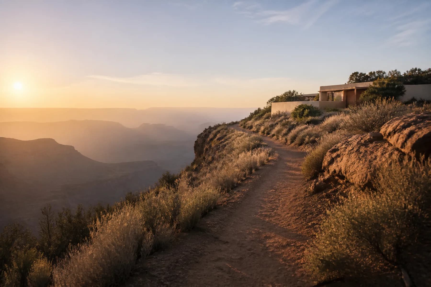 An empty single-track trail contouring along a mesa rim at sunrise