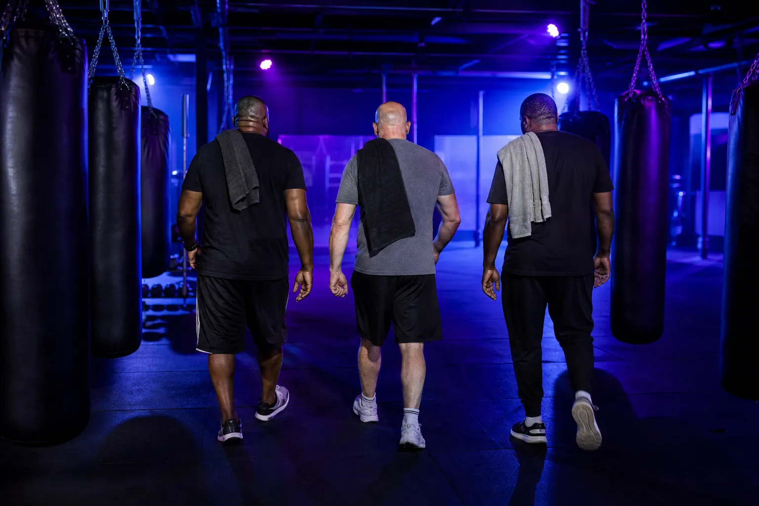 Three coaches seen from behind walking the floor between classes, towels over their shoulders
