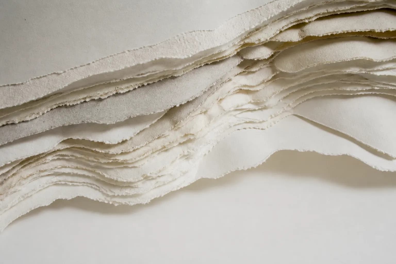 Torn layers of grey and ivory paper revealing strata in cross-section